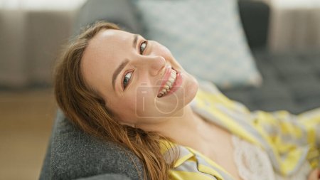 Téléchargez les photos : Jeune femme blonde détendue sur un canapé souriant à la maison - en image libre de droit