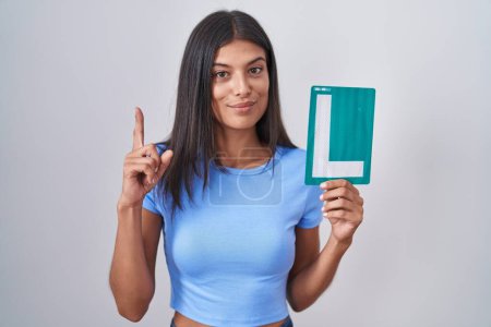 Photo for Brunette young woman holding l sign for new driver surprised with an idea or question pointing finger with happy face, number one - Royalty Free Image