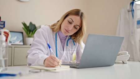 Téléchargez les photos : Jeune belle hispanique femme médecin en utilisant ordinateur portable prendre des notes à la clinique - en image libre de droit