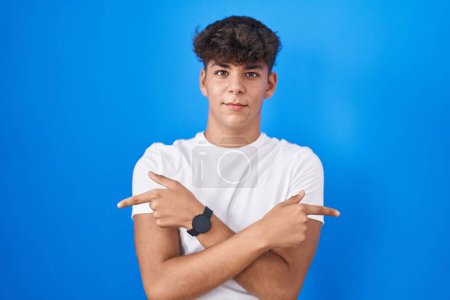 Téléchargez les photos : Adolescent hispanique debout sur fond bleu pointant des deux côtés avec les doigts, direction différente en désaccord - en image libre de droit