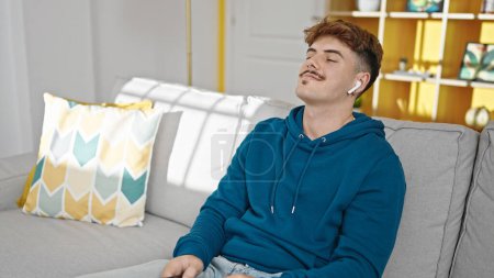 Téléchargez les photos : Jeune homme hispanique écoutant de la musique détendue sur le canapé à la maison - en image libre de droit