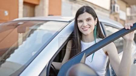 Téléchargez les photos : Jeune belle hispanique femme souriante confiante ouverture porte de voiture à la rue - en image libre de droit