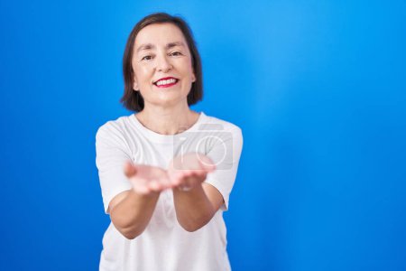 Photo for Middle age hispanic woman standing over blue background smiling with hands palms together receiving or giving gesture. hold and protection - Royalty Free Image