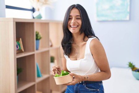 Photo for Brunette woman eating a salad at home smiling and laughing hard out loud because funny crazy joke. - Royalty Free Image