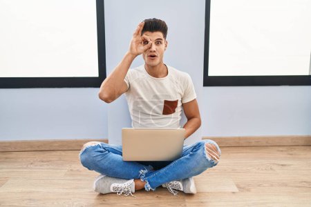 Photo for Young hispanic man using laptop at home doing ok gesture shocked with surprised face, eye looking through fingers. unbelieving expression. - Royalty Free Image