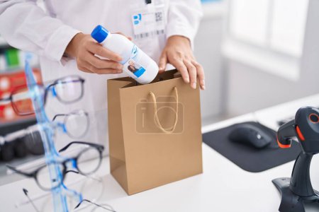 Photo for Young blonde woman pharmacist putting bottle on bag at pharmacy - Royalty Free Image