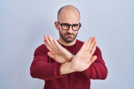 Photo for Young bald man with beard standing over white background wearing glasses rejection expression crossing arms and palms doing negative sign, angry face - Royalty Free Image