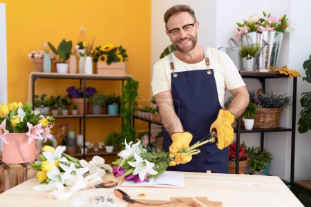Téléchargez les photos : Moyen Age homme fleuriste souriant confiant tige de coupe plante à la boutique de fleurs - en image libre de droit