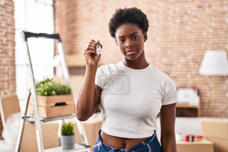 Femme afro-américaine tenant les clés de la nouvelle attitude de pensée à la maison et l'expression sobre regardant avec confiance en soi 