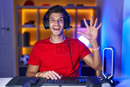 Photo for Young hispanic man playing video games showing and pointing up with fingers number five while smiling confident and happy. - Royalty Free Image