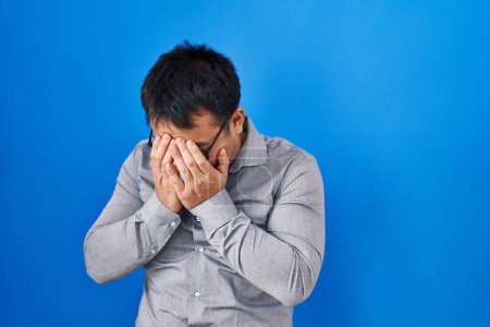 Photo for Young chinese man standing over blue background with sad expression covering face with hands while crying. depression concept. - Royalty Free Image