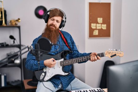 Téléchargez les photos : Jeune rousse homme musicien chantant chanson jouant de la guitare électrique au studio de musique - en image libre de droit
