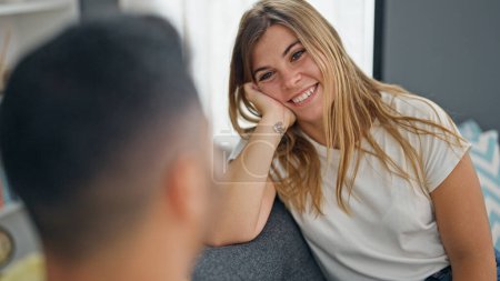 Photo for Man and woman couple sitting on sofa together looking each other at home - Royalty Free Image
