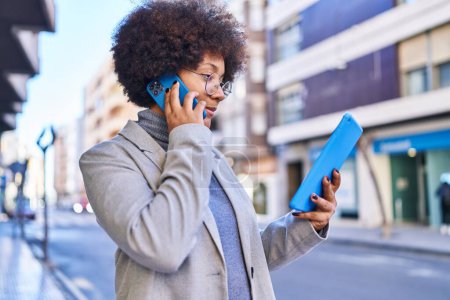 Téléchargez les photos : Afro-américaine femme cadre parler sur smartphone en utilisant touchpad à la rue - en image libre de droit
