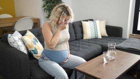 Foto de Mujer embarazada joven sentada en el sofá sufriendo náuseas en casa - Imagen libre de derechos