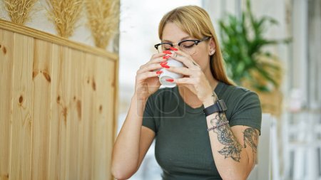 Foto de Mujer rubia joven bebiendo café sentado en la mesa en la cafetería - Imagen libre de derechos