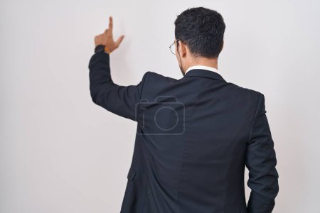 Foto de Hombre hispano de negocios guapo de pie sobre fondo blanco posando hacia atrás apuntando hacia adelante con la mano del dedo - Imagen libre de derechos