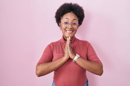 Photo for Beautiful african woman with curly hair standing over pink background praying with hands together asking for forgiveness smiling confident. - Royalty Free Image