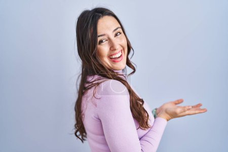 Photo for Young brunette woman standing over blue background pointing aside with hands open palms showing copy space, presenting advertisement smiling excited happy - Royalty Free Image