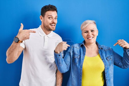 Photo for Young brazilian mother and son standing over blue background looking confident with smile on face, pointing oneself with fingers proud and happy. - Royalty Free Image