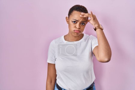 Téléchargez les photos : Belle femme afro-américaine debout sur fond rose inquiète et stressée par un problème avec la main sur le front, nerveuse et anxieuse de crise - en image libre de droit