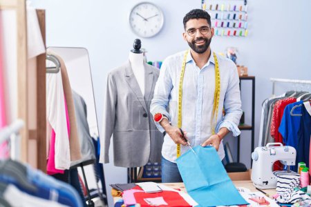 Photo for Young arab man tailor smiling confident cutting cloth at tailor shop - Royalty Free Image