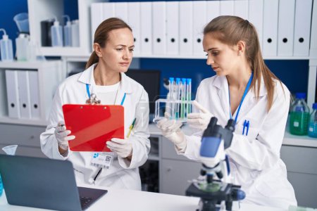 Téléchargez les photos : Two women scientists write on document holding test tubes at laboratory - en image libre de droit