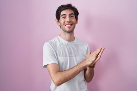 Téléchargez les photos : Jeune homme hispanique debout sur fond rose applaudissant et applaudissant heureux et joyeux, souriant mains fiers ensemble - en image libre de droit
