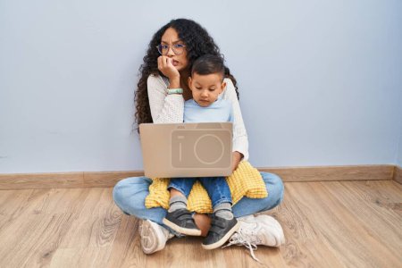 Photo for Young hispanic mother and kid using computer laptop sitting on the floor looking stressed and nervous with hands on mouth biting nails. anxiety problem. - Royalty Free Image