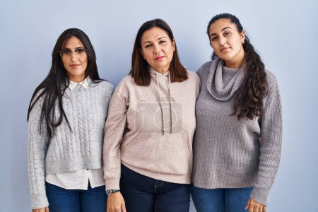 Photo for Mother and two daughters standing over blue background relaxed with serious expression on face. simple and natural looking at the camera. - Royalty Free Image