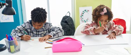 Foto de Adorables estudiantes afroamericanos de niños y niñas sentados en la mesa dibujando en un cuaderno en el aula - Imagen libre de derechos