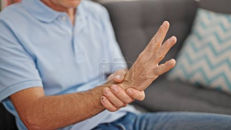 Photo for Middle age man sitting on sofa suffering for wrist pain at home - Royalty Free Image