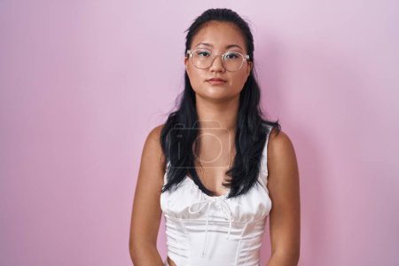 Photo for Asian young woman standing over pink background with serious expression on face. simple and natural looking at the camera. - Royalty Free Image
