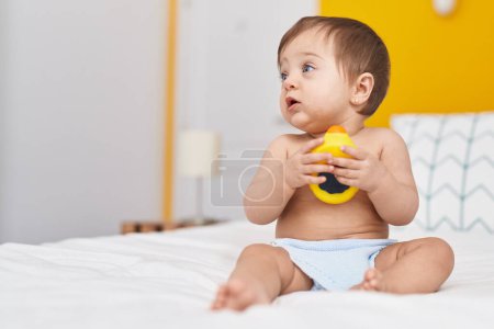 Photo for Adorable caucasian baby sitting on bed playing with duck toy at bedroom - Royalty Free Image