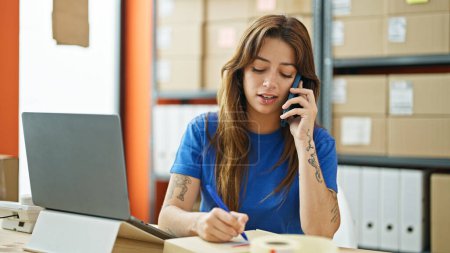 Téléchargez les photos : Jeune belle hispanique femme ecommerce travailleur d'affaires parler sur smartphone écriture sur paquet au bureau - en image libre de droit
