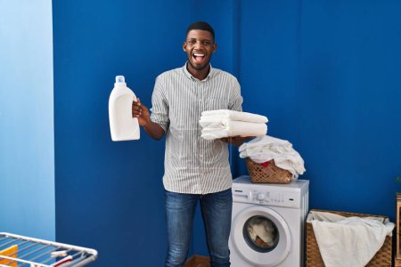 Téléchargez les photos : Afro-Américain tenant des serviettes propres souriant et riant fort à haute voix parce que drôle blague folle. - en image libre de droit