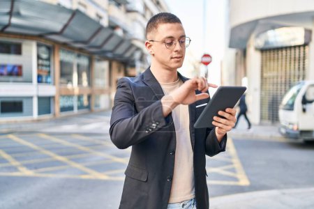 Téléchargez les photos : Jeune homme hispanique exécutif utilisant touchpad avec une expression sérieuse dans la rue - en image libre de droit