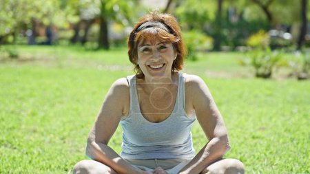 Photo for Middle age woman sitting on yoga mat smiling at park - Royalty Free Image