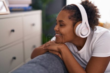 Téléchargez les photos : Femme afro-américaine écoutant de la musique assise sur le canapé à la maison - en image libre de droit