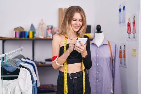 Téléchargez les photos : Jeune femme blonde tailleur souriant écriture confiante sur ordinateur portable au magasin de tailleur - en image libre de droit