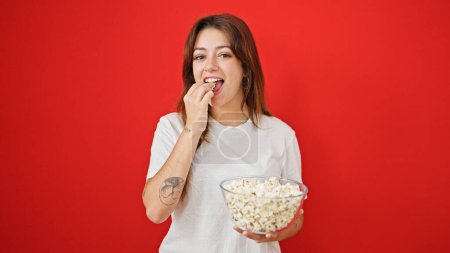 Téléchargez les photos : Jeune belle femme hispanique mangeant du pop-corn souriant sur fond rouge isolé - en image libre de droit