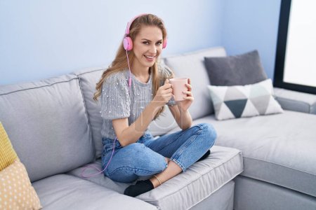 Téléchargez les photos : Jeune femme blonde écoutant de la musique boire du café à la maison - en image libre de droit