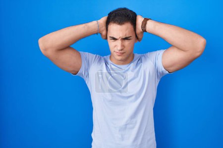 Téléchargez les photos : Young hispanic man standing over blue background suffering from headache desperate and stressed because pain and migraine. hands on head. - en image libre de droit