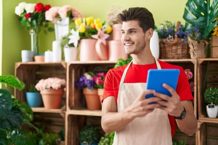 Téléchargez les photos : Jeune homme hispanique fleuriste souriant confiant en utilisant le pavé tactile à la boutique de fleurs - en image libre de droit