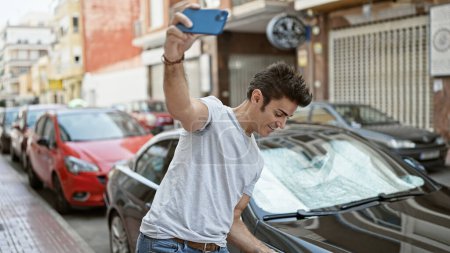 Téléchargez les photos : Jeune homme hispanique faire selfie par smartphone debout en voiture à la rue - en image libre de droit