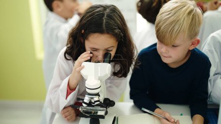 Téléchargez les photos : Adorable garçon et fille élèves en utilisant des notes de microscope écriture à la salle de classe de laboratoire - en image libre de droit