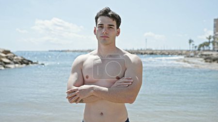 Foto de Joven turista hispano de pie con expresión relajada y brazos cruzados gesto en la playa - Imagen libre de derechos