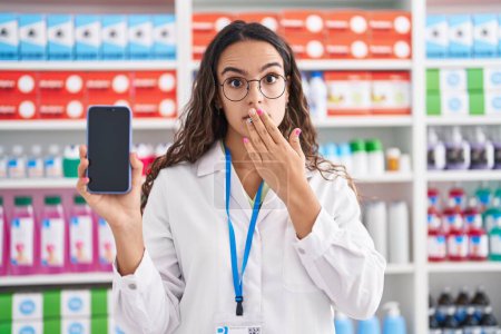 Photo for Young hispanic woman working at pharmacy drugstore showing smartphone screen looking at the camera blowing a kiss being lovely and sexy. love expression. - Royalty Free Image