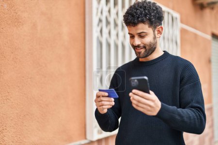 Téléchargez les photos : Jeune homme arabe utilisant smartphone et carte de crédit à la rue - en image libre de droit