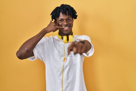 Photo for Young african man with dreadlocks standing over yellow background smiling doing talking on the telephone gesture and pointing to you. call me. - Royalty Free Image